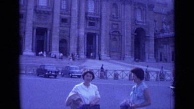 1962: two women speak while standing on wide road by large stone building ROME
