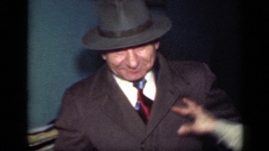 1949: two men and woman inside of home, both men are in suit and tie