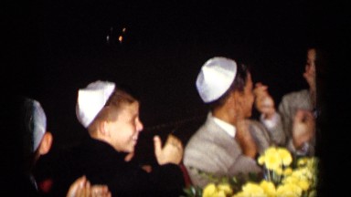 1957: young white boys clapping in suits wearing white yarmulkes seated around