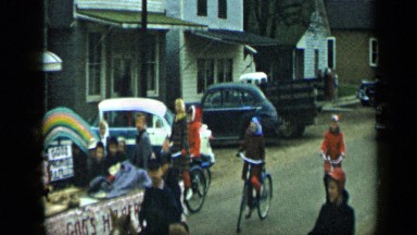 1959: lots of people riding bicycles and car is following them slowly on road