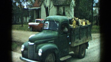 1959: vehicles driving in line carrying wood chunks on unpaved track behind