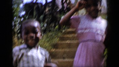 1959: siblings outside house, at bottom of steps waving and smiling VENEZUELA