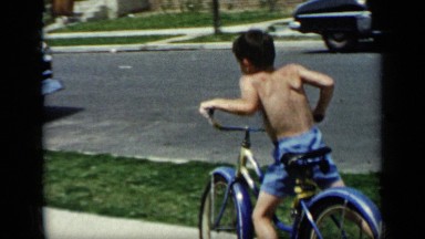 1948: boy in blue shorts riding bicycle down sidewalk and then coming back again
