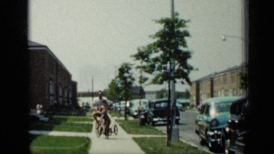 1948: men riding bicycle with his kid sitting in front alongside road NEW YORK