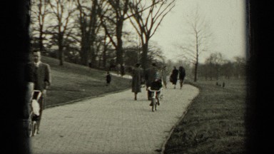 1949: Boy Riding Bike on Walkway in Park While People Pass By
