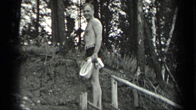 1939: man in bathers walks along a beach throws rocks and chops wood. LONG LAKE