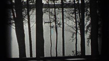 1939: small canoe moving through the lake viewed through the silhouetted trees