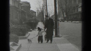 1947: father and daughter take the puppy for a stroll along the sidewalk.