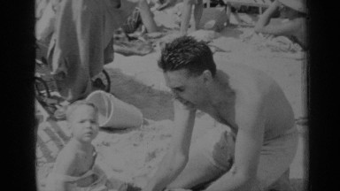 1947: father showing baby how to put sand in a bucket at the beach NEW YORK