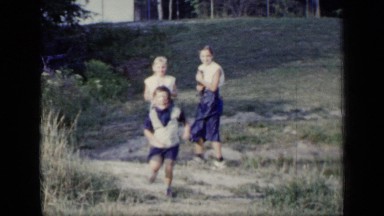 1948: young boy and girl run toward the camera while a teen holds a kitten