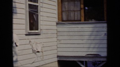 1948: family sit on the porch of a house while a young child runs