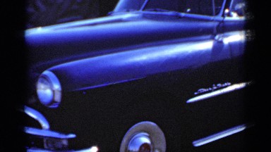 1950: a man in the driver's side of a car, backing out of a parking space