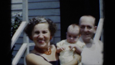 1950: grandmother hold grandchild while her husband touches the baby's head.