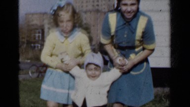 1950: two sisters help their brother walk by holding his arms up on either side