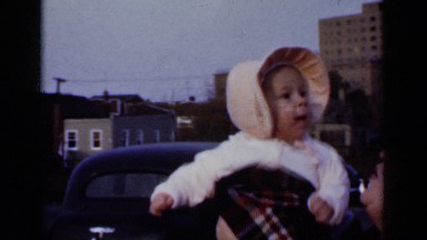 1950: a woman on a busy street holding her baby in the air. NEW YORK