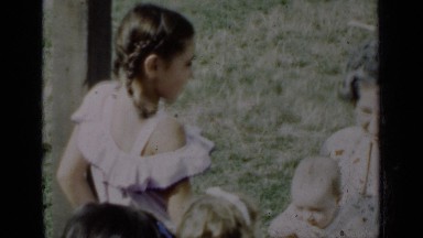 1950: a older woman sitting in the grass holding a baby while talking to a group