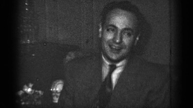 1950: smiling man in a suit talking and pulling up his pant leg NEW YORK