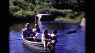 1951: a young boy paddle a small group of people in a row boat on the water
