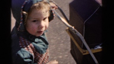 1951: a young child has fun pushing a pram on a quiet road. NEW YORK