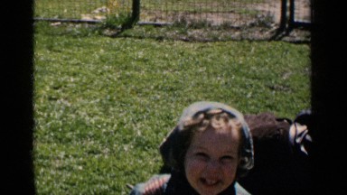 1951: a kid and another person playing with dog in the grasses within the gate