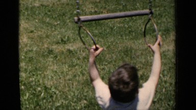 1951: young boy smiling and playing with gymnastic rings on a swing set outdoors