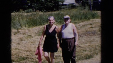 1951: an older couple walks down the road towards the camera, a young boy joins
