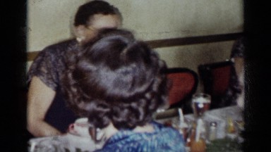 1954: men, women and children sitting at a table eating a meal and talking.