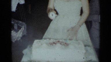 1954: bride in wedding gown blows out candles on wedding cake