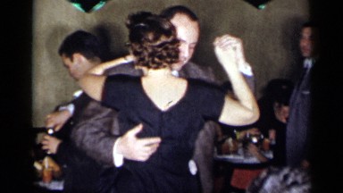 1954: a man and woman dancing at an event with people sitting at a table