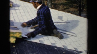 1957: dark skin man nailing tiles together outside with a hammer. BIRMINGHAM