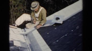 1957: a carpenter sitting on the roof and fixing the channel for water