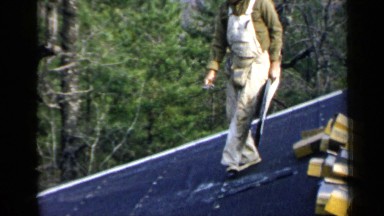 1957: various workers atop a structure with tools installing shingles
