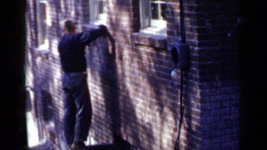 1957: man stands on partition and leans against building to sand brick wall
