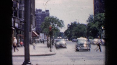 1957: the street of a town in the daytime with many vehicles and pedestrians