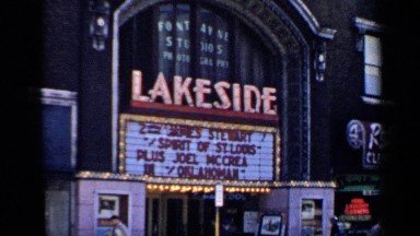 1957: near the lakeside buildings,there are few peoples are walking through