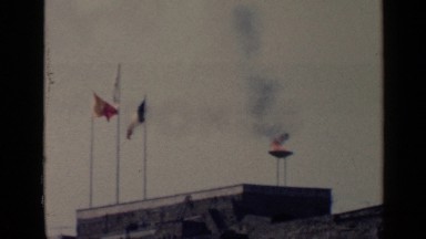 1960: countries flag flying high with fire in the background on a sunny day ROME
