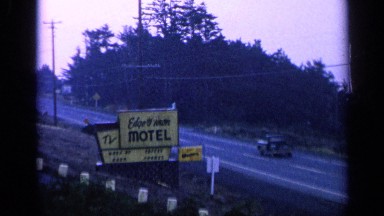 1963: Camera Pans Along Sunset Shot of Motel Signs, Road and Trees. California