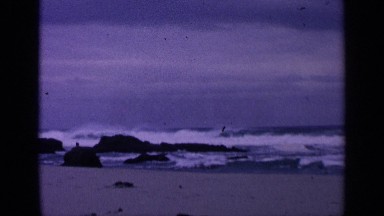 1963: white cap waves gently crashing against beach rocks under slightly stormy
