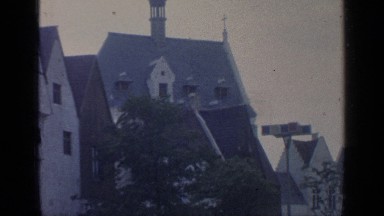 1964: wind blows trees growing in front of buildings with steep roofs