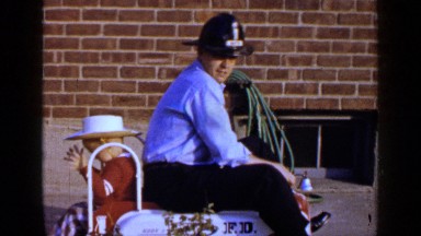 1965: father and son play together on a toy truck as father is dressed