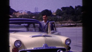 1965: man in suit stands beside vintage car before getting in. LONG ISLAND
