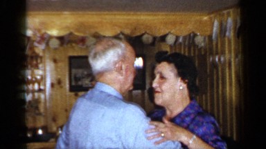 1965: elderly couple dance around living room while friends watch on.