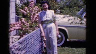 1965: a woman standing by a chain link fence in the front yard LONG ISLAND