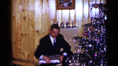1965: a man opening a christmas present in front of the christmas tree