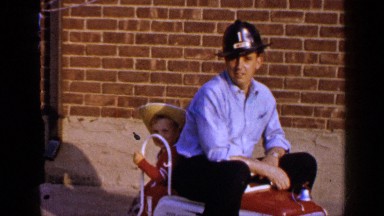 1965: A Man and His Son Sitting on a Child-Sized Fire Truck