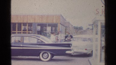 1961: A Small Group of People Standing Outside in a Parking Lot Between Cars