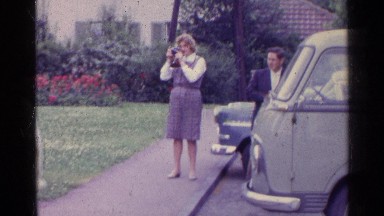 1961: Woman Taking Pictures Beside Cars and Groups of People and Children