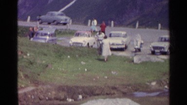 1961: Parked Cars with People Standing and Walking on Grass in Switzerland