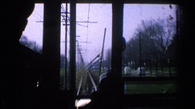1965: man driving train outside on the track and looking at the cars driving by