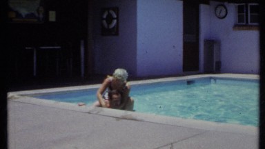 1971: woman rides on man's back as he wades along edge of outdoor pool